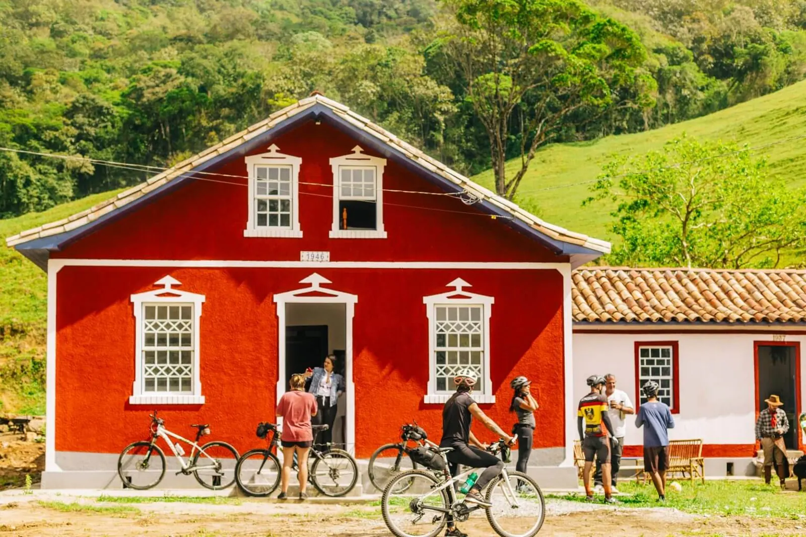Ciclistas parados diante de uma casa rural vermelha