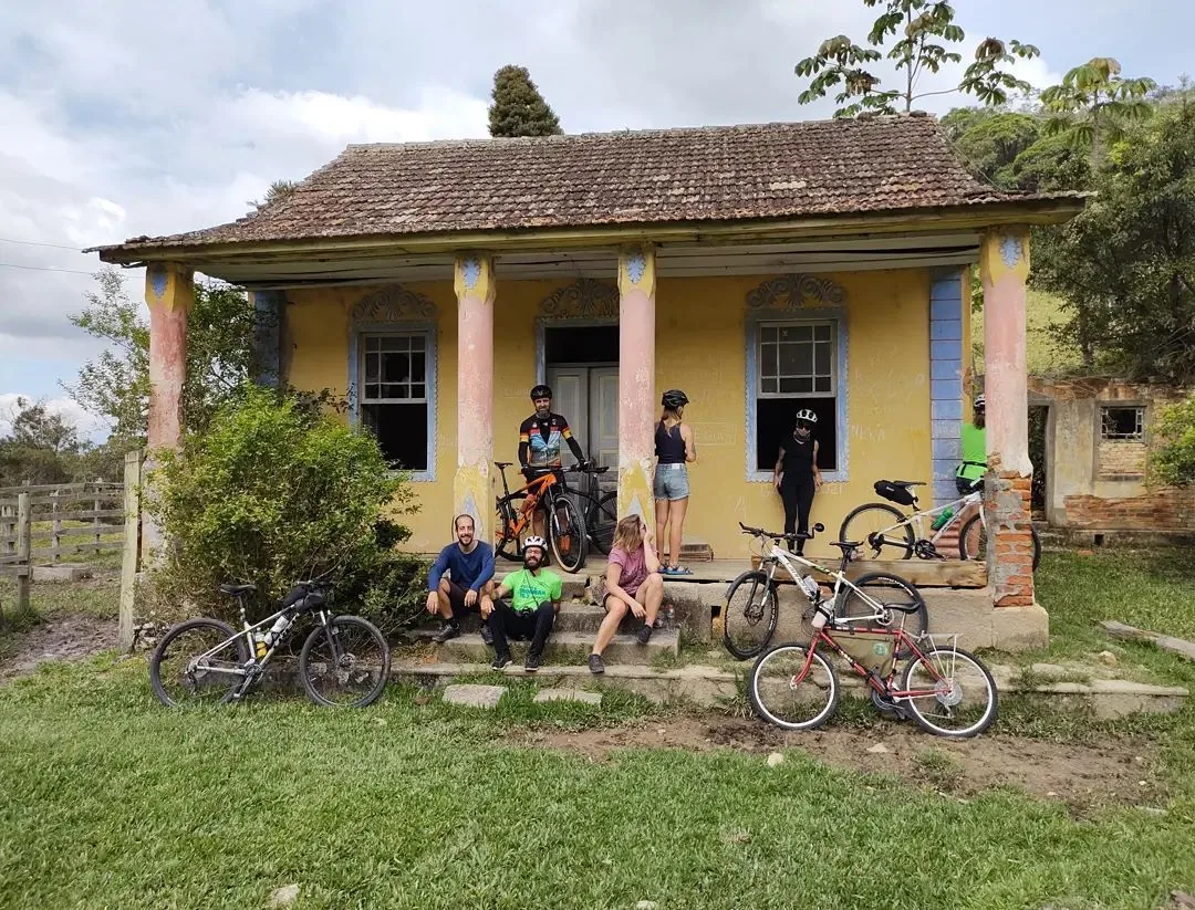 Ciclistas diante de uma casa antiga durante a passagem pela Trilha das Bruxas