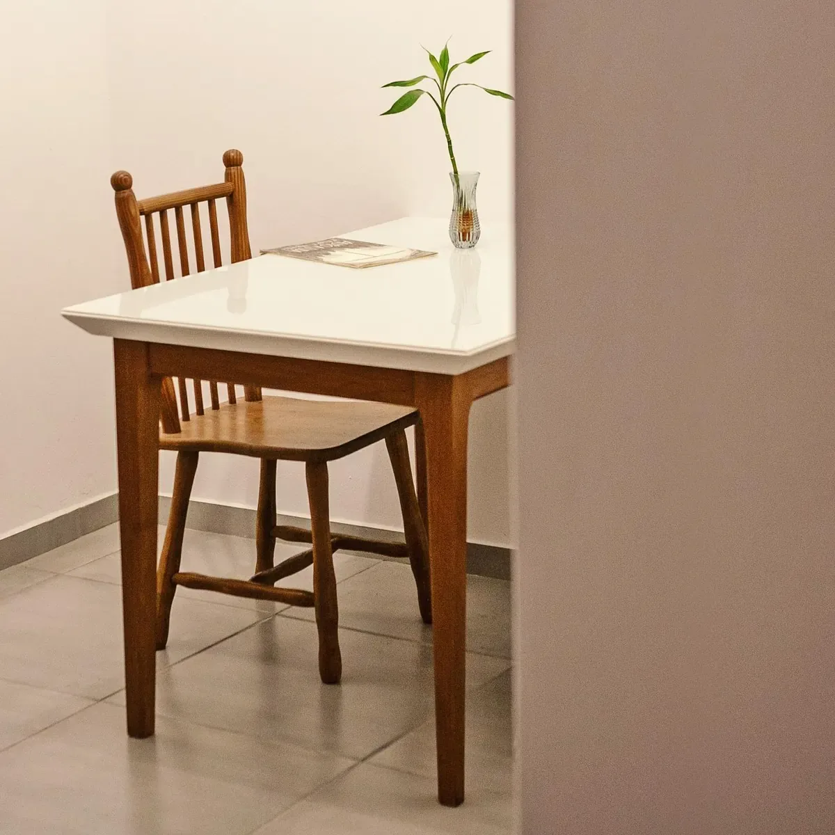 Mesa branca com cadeira de madeira e uma muda em garrafa de vidro no apartamento 403