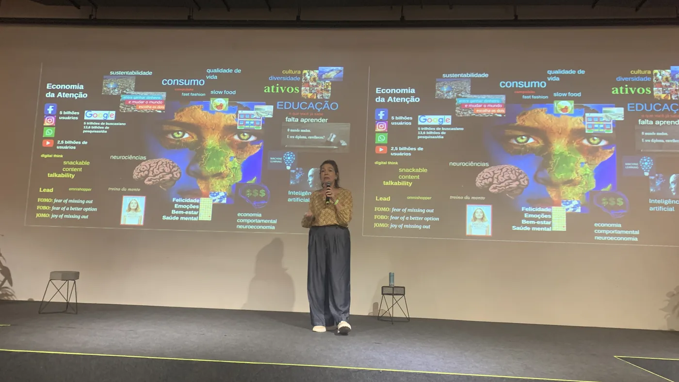 Regina Migliori, do MindEduca, apresentando o slide sobre a economia da atenção, com termos como FOMO, FOBO e JOMO ao lado de uma imagem de cérebro