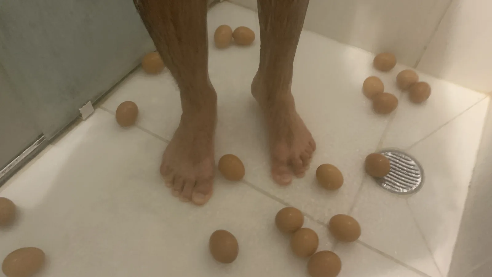 Vista de cima dos pés do autor cercados de ovos espalhados sobre o piso molhado do banheiro