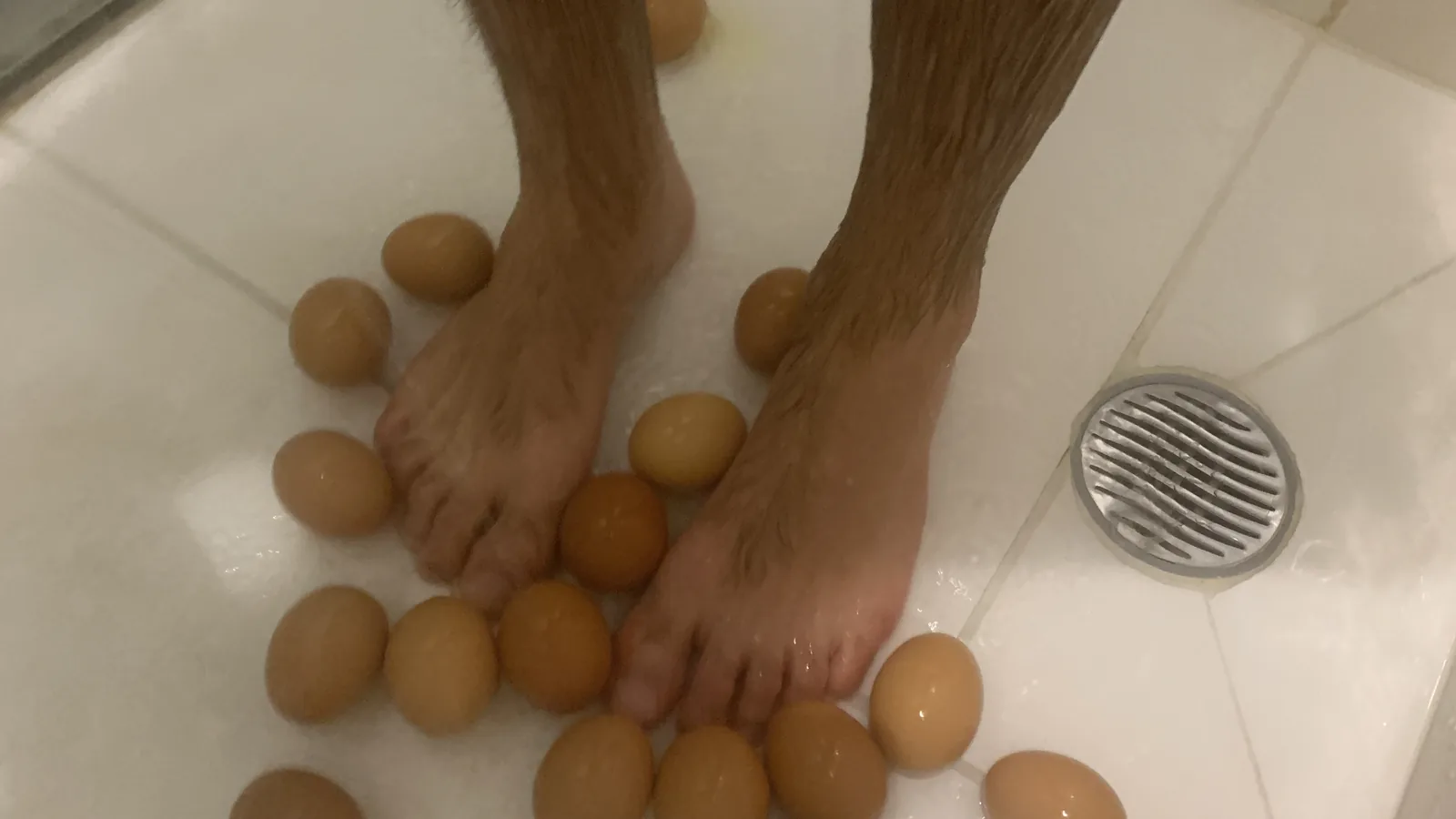 Pés do autor entre dezenas de ovos molhados no chão do chuveiro, próximos ao ralo