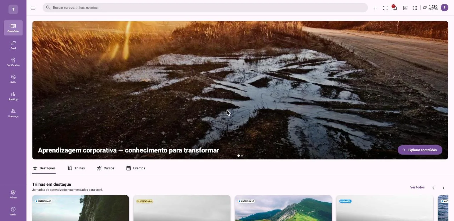 Captura da tela inicial de uma plataforma de aprendizagem com menu lateral roxo, campo de busca, banner com estrada de terra ao entardecer e cards de trilhas em destaque.