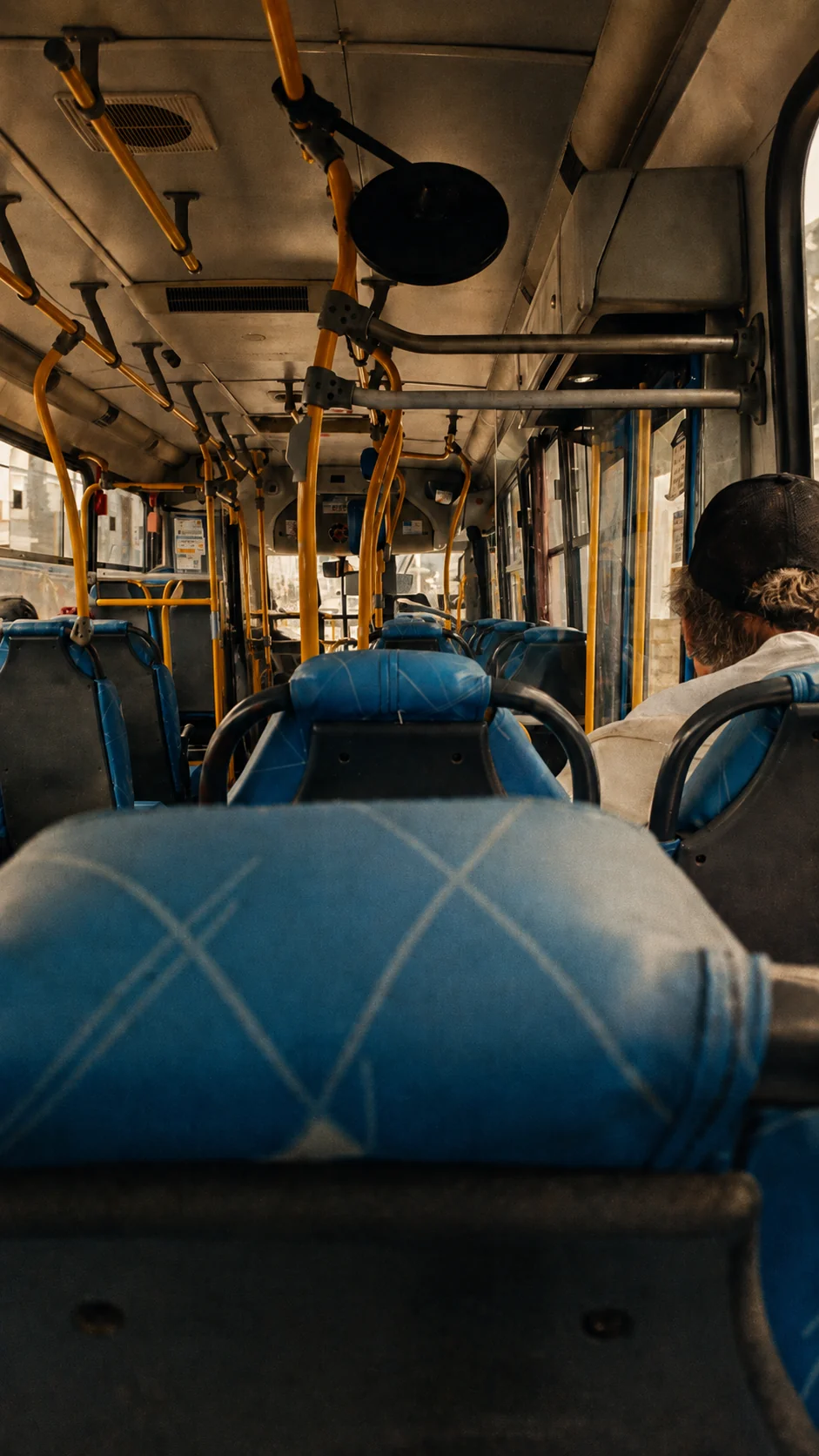 Interior de um ônibus visto de trás, entre bancos azuis e barras amarelas