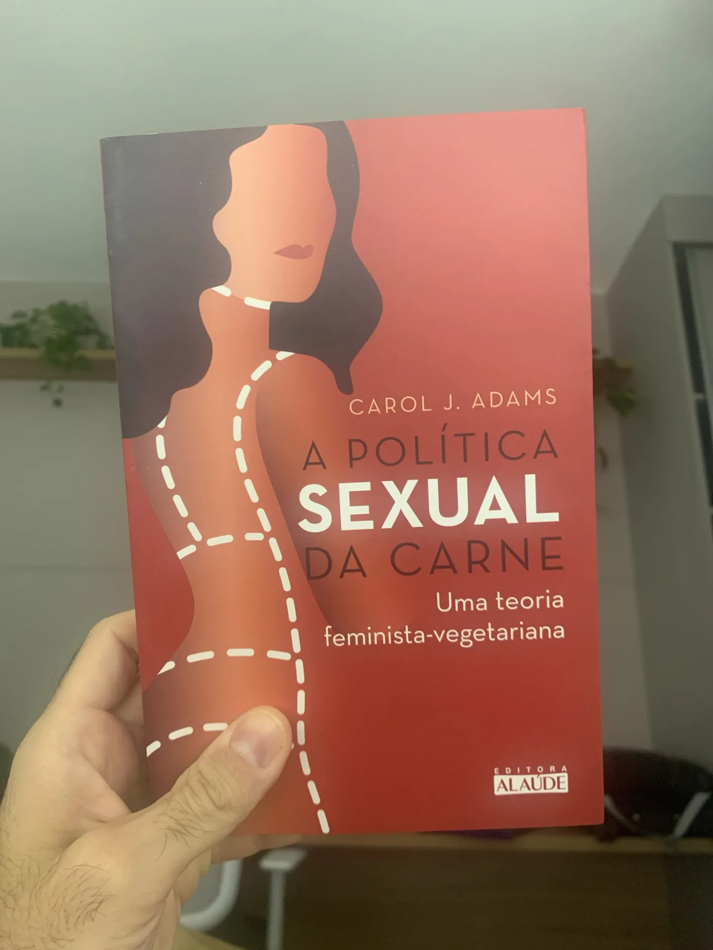 Foto do livro A política sexual da carne, de Carol J. Adams, segurado pela mão do autor diante de uma parede clara.