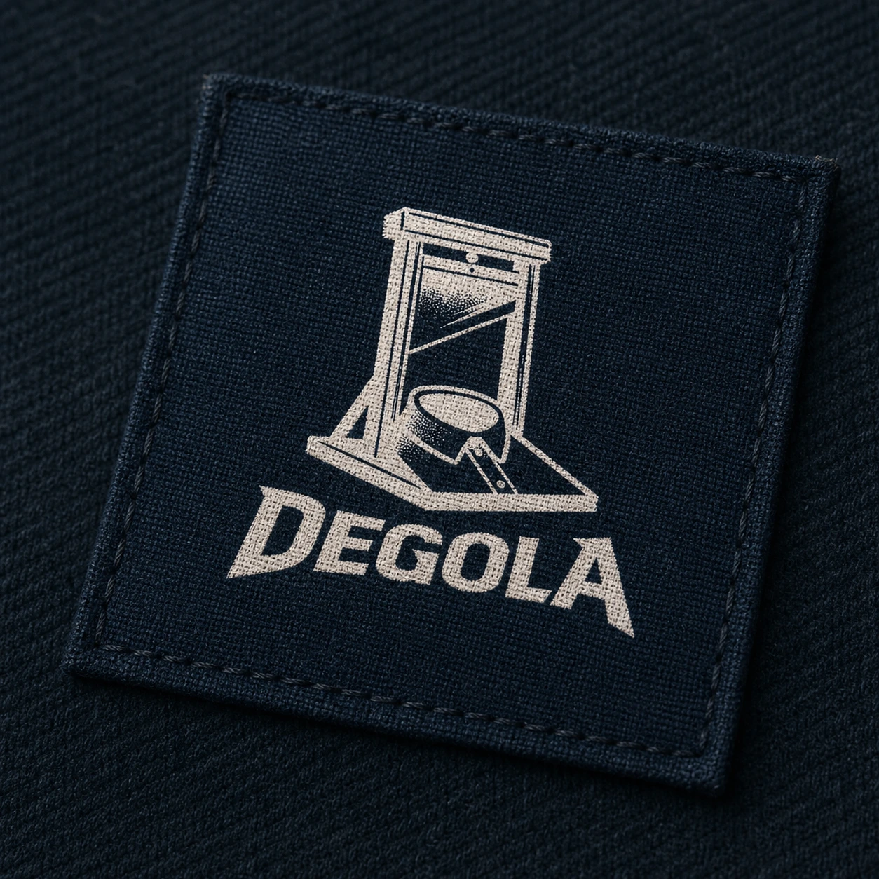Aplicação negativa da marca Degola em patch têxtil petrol com o logotipo bordado em branco